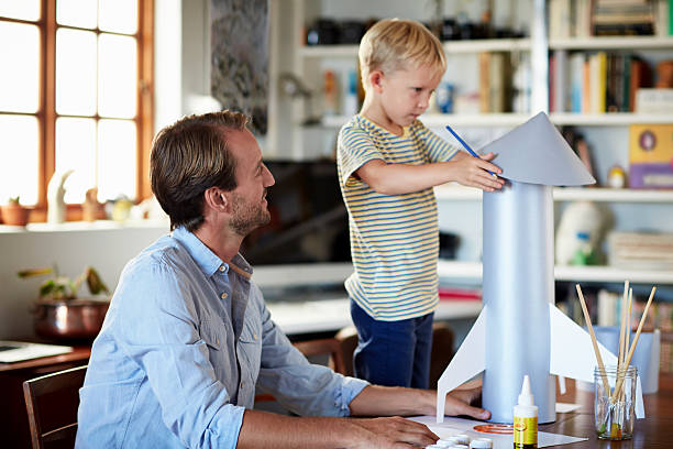 Father and son building rocket at table in living room